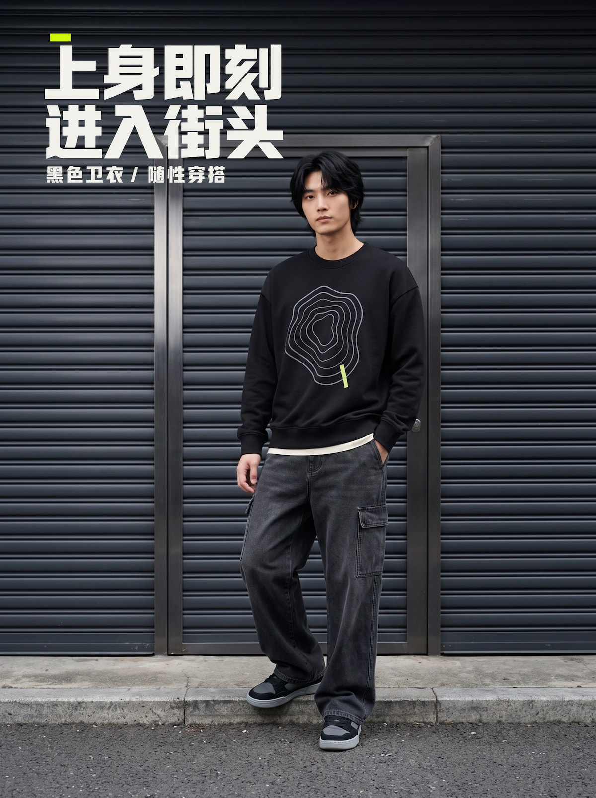 黑发男模特在深灰卷帘门街景前穿原创印花黑色卫衣、水洗宽松工装裤与板鞋